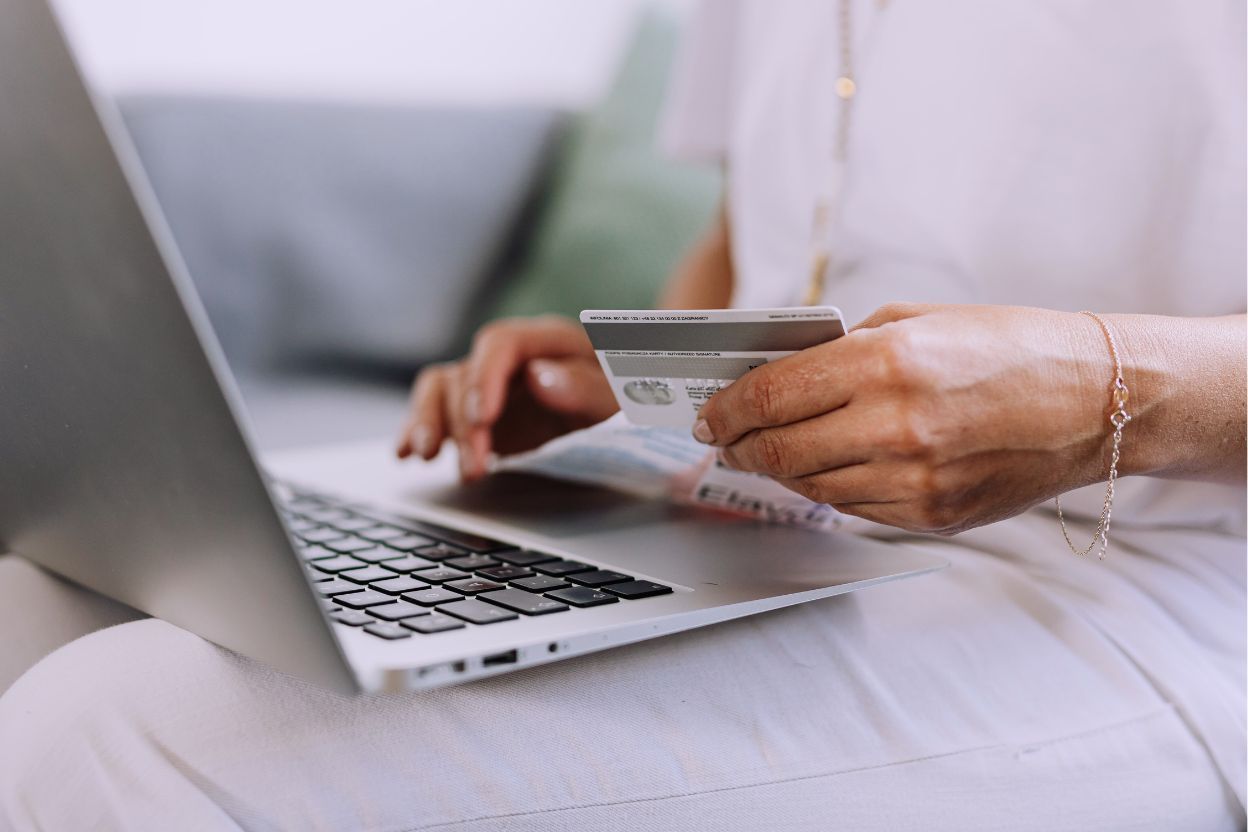 Человек за ноутбуком держит банковскую карту и выполняет финансовые операции онлайн.