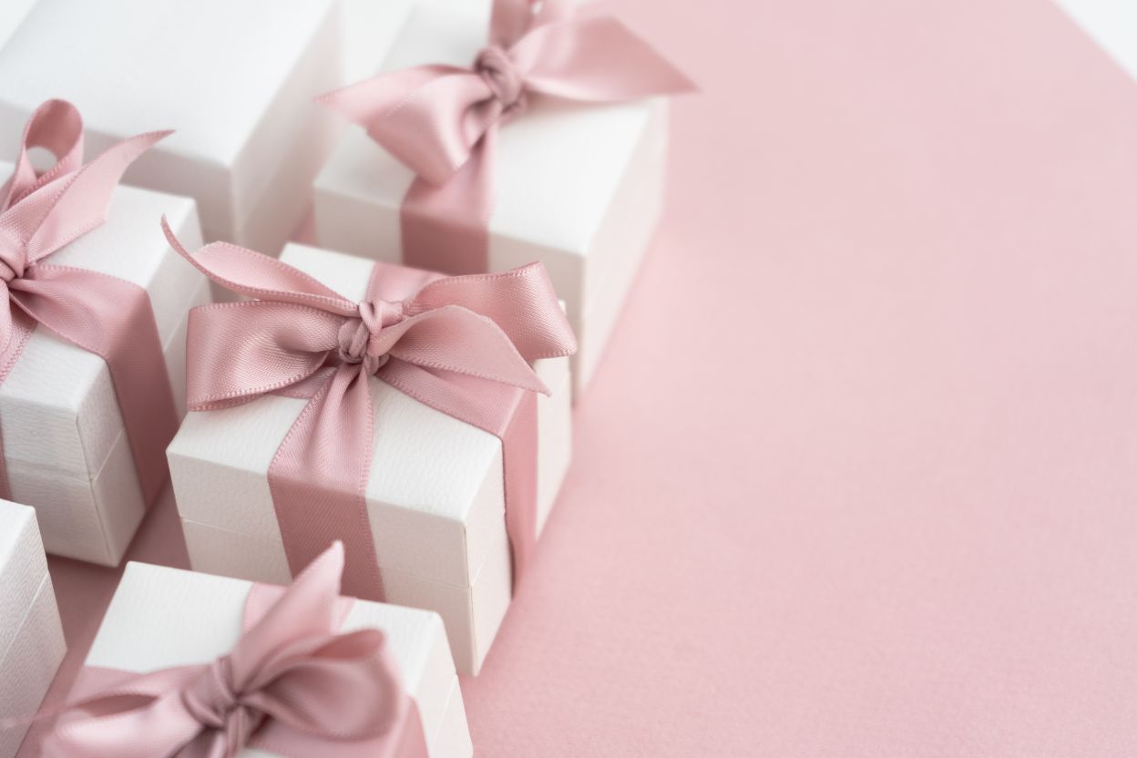 Белые подарочные коробочки с розовыми лентами на розовом фоне